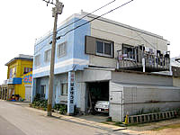 沖永良部島の民宿はまゆう荘 - 水色の建物が目印で、向かいが黄色い酒の安売り店